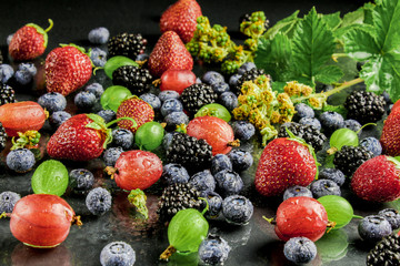 Wet berries. Background of fresh fruits and berries. Ripe blackberries, strawberries, gooseberries, blueberries, arrikos. Background berries and fruits. On a wooden background.