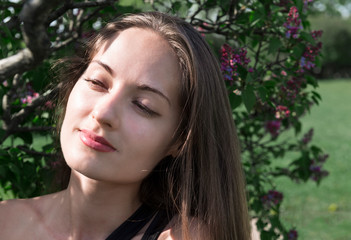 Fototapeta premium portrait of a beautiful girl on a green background, a young woman in nature ,lilac Bush