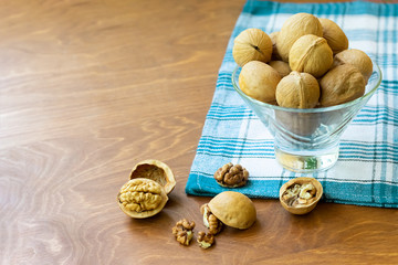 Whole walnuts and walnut kernel halves without shell on a dark wooden table and checkered towel,...
