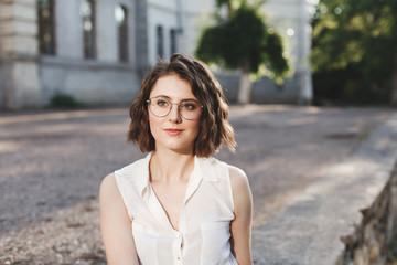 Portrait of beautiful young brunette woman in glasses, outdoors in warm sunny day.