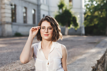 Fototapeta premium Portrait of beautiful young brunette woman in glasses, outdoors in warm sunny day.
