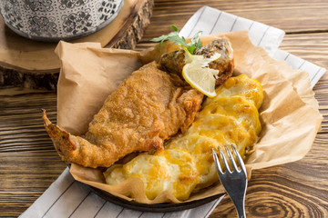 Baked whole dorado in batter with potato and melted cheese on wooden table