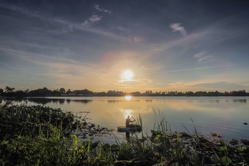Lake view morning of a fisherman floating in water with sunrise background, sunrise at Krajub Reservoir, Ban Pong, Ratchaburi, Thailand.