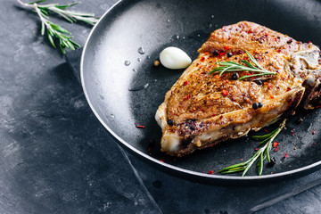 Piece of fried meat with rosemary and garlic in a pan close up