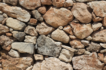 Natural beige stone wall (masonry) created by stacking stones on top of each other with varying stone sizes.