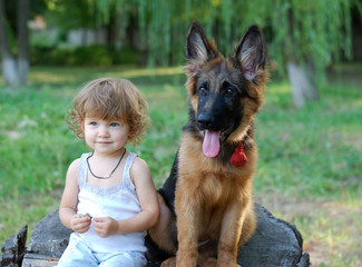 Cute charming toddler girl sitting with german shepherd dog in the park.