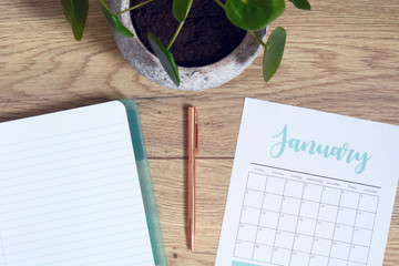 High-angle shot of a home office desk space with a plant, notebook and a calendar with pen