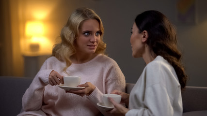 Two female friends drinking tea at home and talking about life, gossiping