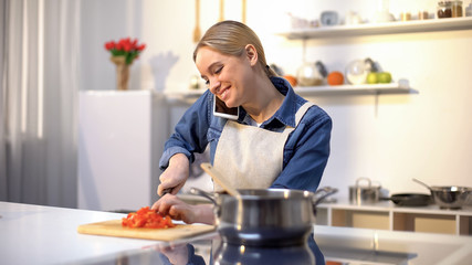 Young woman talking on phone and preparing tomato sauce, easy food recipe