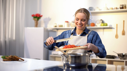Positive girl listening music and cooking vegetables, healthy low-calorie eating