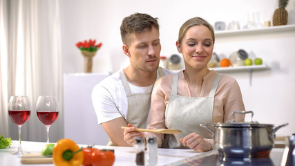 Fototapeta na wymiar Cute couple cooking meal, romantic date at kitchen, glasses of red wine on table