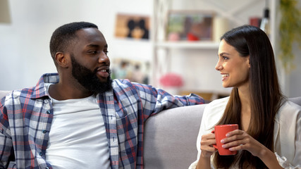 Young mixed-race couple drinking coffee and talking at home, nice conversation