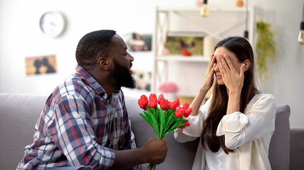 Afro-American man presenting bunch of tulips to Caucasian girl, anniversary gift
