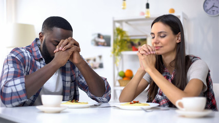 Young multiethnic couple praying before lunch, thanking God for meal, religion
