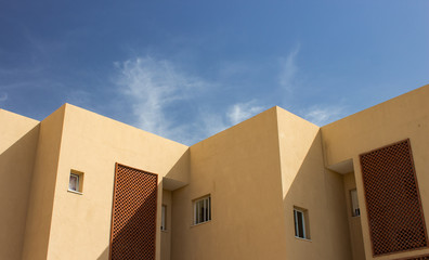 sunny urban style picture of living house yellow concrete walls geometric lines and shapes concept from below on blue sky background