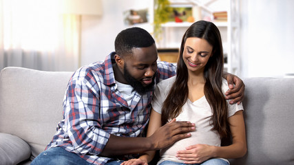 Smiling African-American man stroking his pregnant wife tummy, future parents