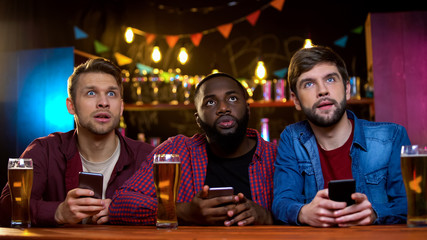 Male friends watching lottery sitting in bar and checking numbers online, bet