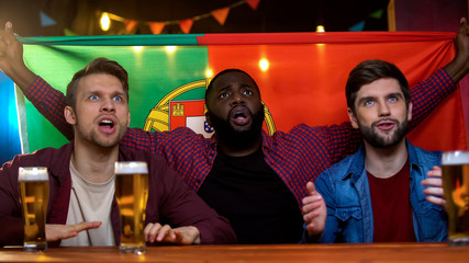 Nervous portuguese fans waiting for decisive kick for soccer team victory, flag