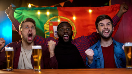 Cheerful portuguese multiracial men celebrating soccer team victory, waving flag