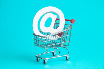 Wooden white email symbol in shopping trolley isolated on blue. Buy online concept.