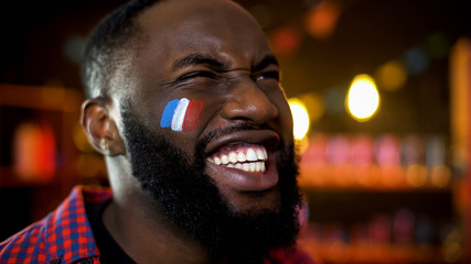 Very emotional black fan with french flag painted on cheek cheering for team - obrazy, fototapety, plakaty
