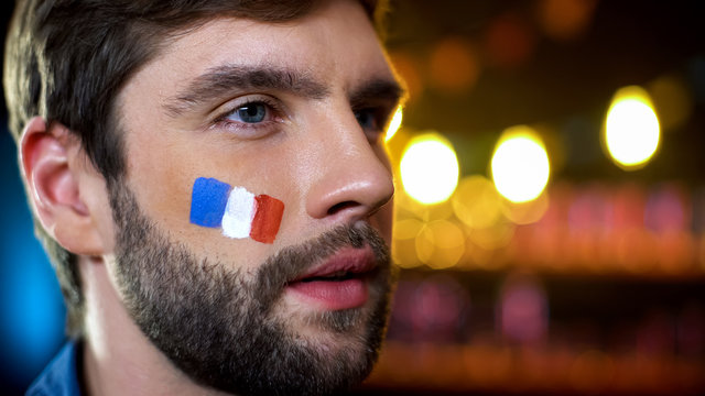 Serious man with painted french flag on cheek watching election results on tv
