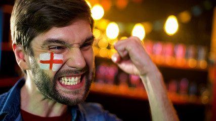 Joyful english football fan with flag on cheek making yes gesture, team winning