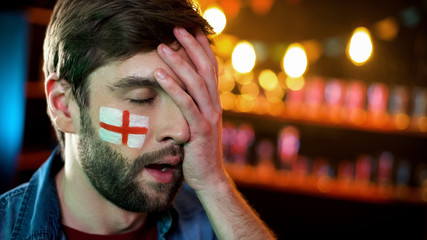 Displeased male football fan with english flag on cheek making facepalm gesture
