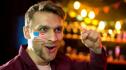 Emotional american football fan with flag on cheek making yes gesture, win