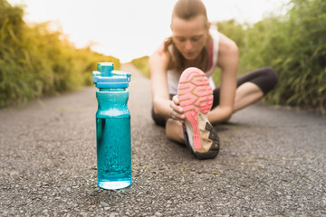 Drinking water and fitness concept. Young female runner stretching next to bottle of water. 