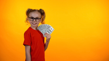 Pretty teenage girl in spectacles showing bunch of dollar bills, earning money