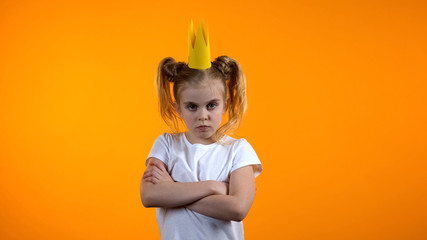 Funny naughty child in princess crown standing with hands crossed on chest