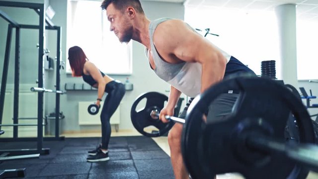 Muscular man and a young woman lifting heavy weights at gym. Fitness couple doing workout in the sport club. Athletic couple finishes the exercise together and puts barbells on floor.