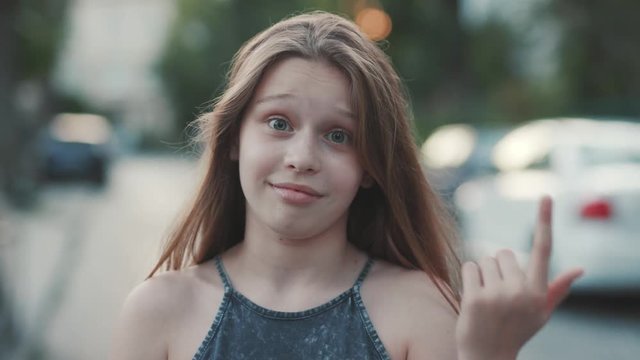 Close-up portrait of nice surprised little girl with long hair. Outdoors. Reaction to strange behavior. Teenager twirling one's finger around one's ear. Outside. Summertime.