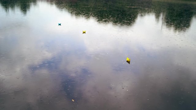 Three colorful paper ships on water under the rain. Handmade origami ships are floating on the water surface during the rain outdoors. Top view.