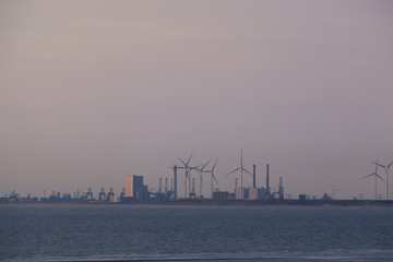 Obraz premium Energy import. Industrial and harbor area in the evening light from a distance. In between wind turbines and water in the foreground.
