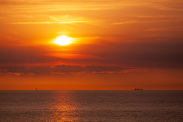 An oil platform and a cargo ship in the sea in the distance on the horizon in the sunset.