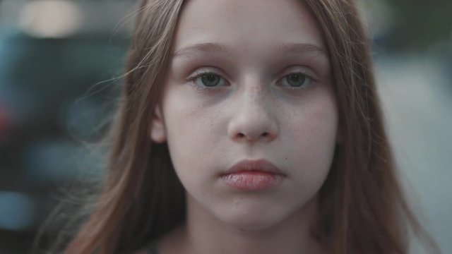 Close-up footage of nice young girl with freckles. Closed eyes. Serious teenager with deep green eyes looking directly at camera. Outside.