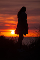 Woman on a dune in the sunset.Silhouette of person and dune grass with low sun and glowing red sky