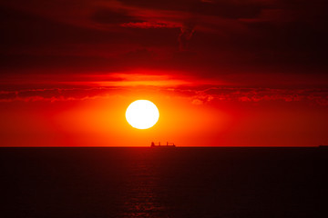Cargo ship on the sea in sunset with  cloud formations in red light