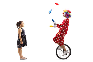 Surprised little girl looking at a clown on a unicycle juggling
