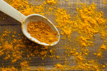 Turmeric powder in wooden spoon on wooden rustic looking table