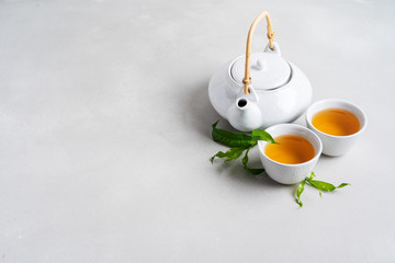 Tea concept with white tea set of cups and teapot surrounded with fresh tea leaves on concrete...