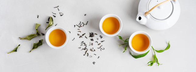 Tea concept with white tea set of cups and teapot surrounded with fresh tea leaves on concrete background with copy space. Long banner.