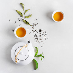 Tea concept with two white cups of tea and teapot surrounded with fresh green tea leaves and dry...