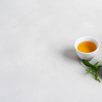 White cup of tea  surrounded with fresh tea leaves on concrete background with copy space.