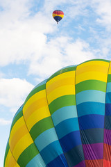 Two hot air balloons floating under vibrant blue sky with puffy white clouds