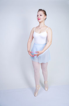 cute caucasian girl in ballet clothes learning to be a ballerina on a white background in the Studio. plus size young woman dreams of being a dancer.