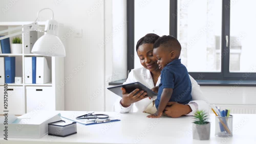 Wall mural medicine, technology and pediatry concept - happy african american female doctor or pediatrician showing tablet computer to baby boy patient at clinic