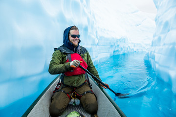 Ice climber paddling through narrow canyon cut through glacier ice, filled with deep blue water.